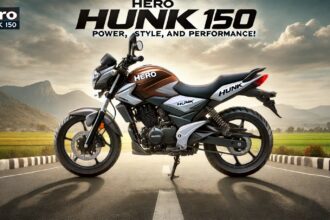 Hero Hunk 150, एक स्पोर्टी और मस्कुलर मोटरसाइकिल, डुअल-टोन बॉडी कलर, एलॉय व्हील्स और LED हेडलाइट्स के साथ, ओपन रोड पर खड़ी हुई। बैकग्राउंड में पहाड़ और नीला आसमान नजर आ रहा है।