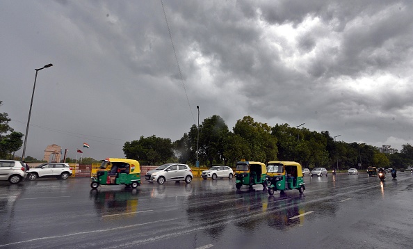 Delhi NCR weather alert: Dark clouds and rain over the city skyline with people using umbrellas.