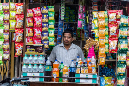 किराना स्टोर में ग्राहक खरीदारी करते हुए, विभिन्न घरेलू वस्तुएं शेल्फ पर सजी हुई